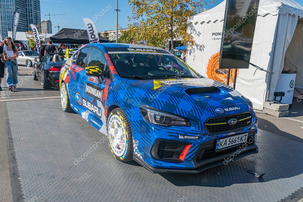 Vibrant blue Subaru race car on a platform, surrounded by tents and other vehicles, in an outdoor event Aerodynamic design with sponsor logos Rocket, Subaru Whit Kyiv, Ukraine - September 21, 2025