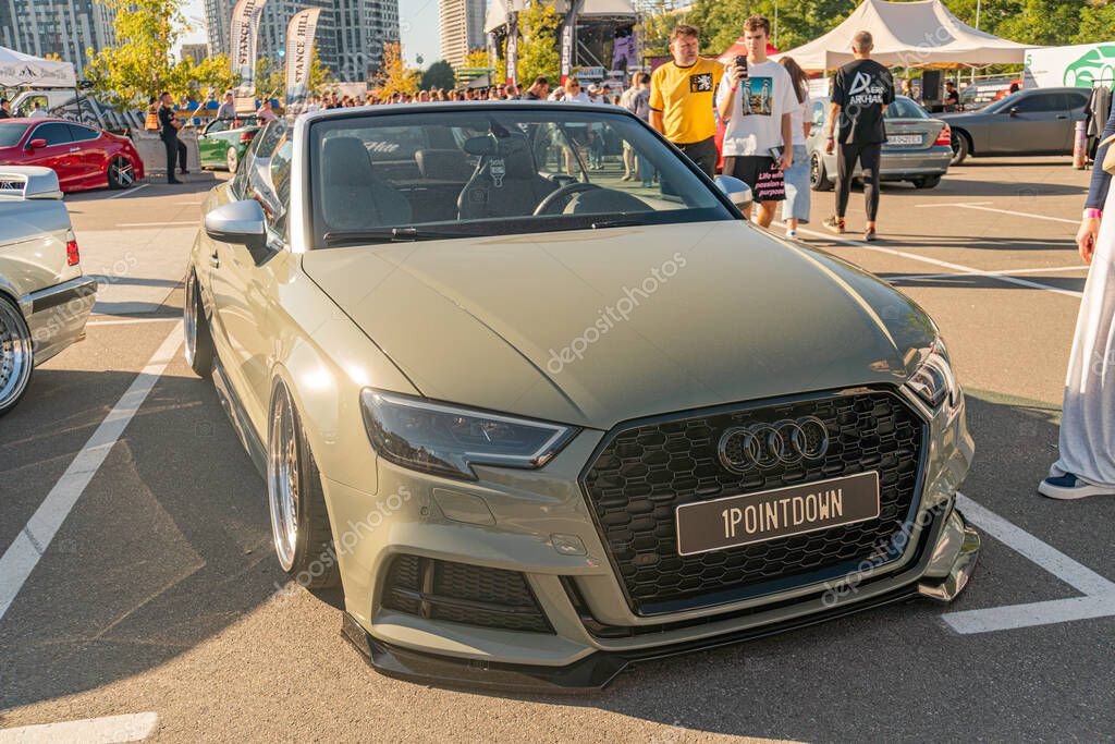 Parked Audi car in a bustling outdoor setting, matte green finish, black grille with Audi logo, alloy wheels, license plate UP THE KNOB, soft natural lighting, bus Kyiv, Ukraine - September 21, 2025