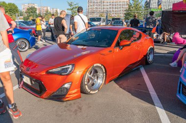 Büyük bir otoparktaki turuncu spor araba, çapraz park halindeki günlük giysiler içindeki birden fazla kişinin dikkatini çekiyor, parlak turuncu kaporta, ac Kyiv, Ukrayna - 21 Eylül 2025