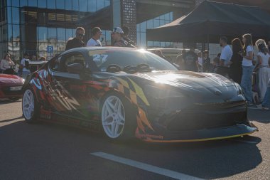 Açık hava yarış pisti, hareketli ortam, turuncu ve kırmızı alev desenli siyah spor araba, güneş ışığını yansıtan parlak dış görünüş, arka planda bir grup izleyici, parlak Kyiv, Ukrayna - 21 Eylül 2025