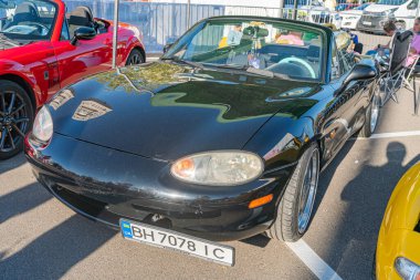 Açık hava otomobil fuarında koyu renkli, bakımlı bir Porsche spor araba muhtemelen Avrupa modeli, ve diğer spor arabalar, parlak doğal aydınlatma altında Kyiv, Ukrayna - 21 Eylül 2025