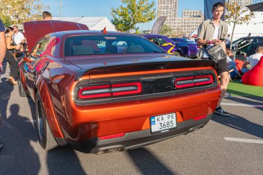 Parlak gün, özel modifikasyonları olan parlak kırmızı-siyah kaslı araba, zıt siyah tekerlekler, iki kalın kırmızı stop lambası, beyaz plaka, arka grup Kyiv, Ukrayna 'da sıradan kalabalık - 21 Eylül 2025