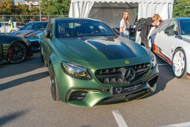 Canlı yeşil bir Mercedes-AMG GT4 yarış arabası, ön tampon ve yan aynalarda sarı aksanlı izleyicilere doğru bakan hareketli bir araba gösterisinde öne çıkıyor.