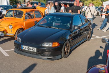 Antika arabalar ve motosikletler gri kaldırımdaki geçici bir otoparkta toplandı, etrafını insanlar sardı. Masa süsleri klasik tasarımla parıldayan siyah bir araba, I Kyiv, Ukrayna - 21 Eylül 2025