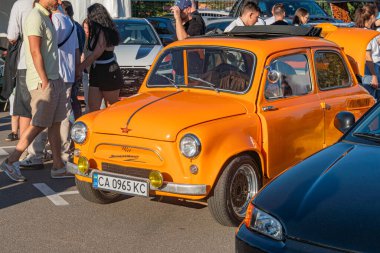 Sarı şeritli turuncu renkli araba, gündüz araba park yerinde çapraz park halinde. Arka plandaki arabaların çeşitliliği Asfalt zeminde. Doğal gün ışığı.