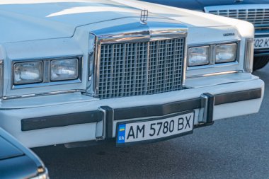 Gece bir şehir caddesinde klasik beyaz bir arabanın yakın plan görüntüsü başka bir araç tarafından kısmen gizlenmiş Kiev, Ukrayna 'nın zarif ızgarasından yansıyan yapay ışıklandırma - 21 Eylül 2025