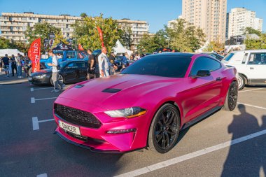 Siyah yarış çizgileri ve özel jantları olan parlak pembe Ford Mustang kaslı araba, şehir sokaklarında mavi aksanlı beyaz bir binanın zeminine park edilmiş ve g Kyiv, Ukrayna - 21 Eylül 2025