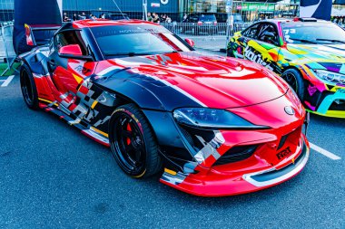 Pistte kırmızı ve siyah Toyota Supra yarış arabası, kaygan lastikler ve aerodinamik parçalarla donatılmış, yarış ortamında diğer arabalarla çevrili, Ukrayna 'nın başkenti Kyiv' in bulutları altında, 21 Eylül 2025