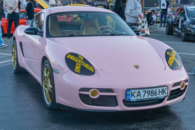 Bir otomobil fuarında pembe Porsche spor arabası, sarı farlar ve altın jantlar, doğal gün ışığı altında, samimi perspektif Kyiv, Ukrayna - 21 Eylül 2025