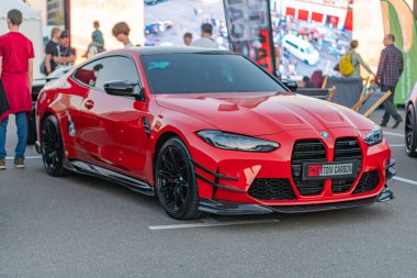 Kırmızı bir BMW 'nin köşegen park ettiği canlı, kentsel bir sokak sahnesi güneş ışığını yansıtan insanlar ve arka plandaki beton sokakta beyaz çizgilerle yapılan hareketlilik ama Kyiv, Ukrayna - 21 Eylül 2025