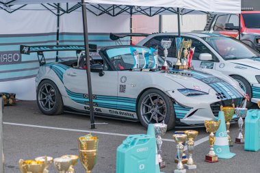 Beyaz bir çadırın altında iki yarış arabası, biri mavi diğeri turuncu, her ikisi de çeşitli yarışlardaki zaferleri simgeleyen ödüllerle süslenmiş, Kyiv, Ukrayna - 21 Eylül 2025