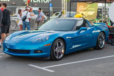 Siyah alçak çatılı canlı mavi Corvette, açık hava otomobil etkinliği veya sergi merkezine park edilmiş insanlar, doğal ışıklandırma, açılı perspektif Kyiv, Ukrayna - 21 Eylül 2025
