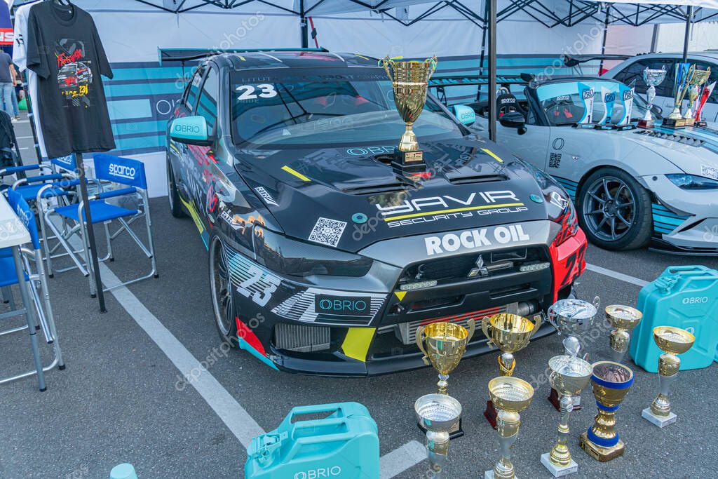 Black racing car on a concrete surface with scattered trophies, parked at a trackside compound Car is well-maintained and has sponsor logos Blue tent visible behin Kyiv, Ukraine - September 21, 2025