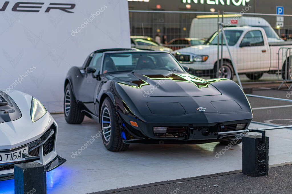 Two sports cars, white modern Corvette with angular headlights and sleek design, black traditional muscle car both on elevated display platform at a car show or exh Kyiv, Ukraine - September 21, 2025