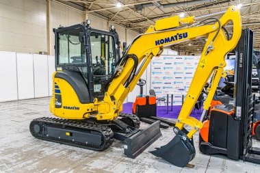 Sarı Komatsu kazıcısı, beton zemine yerleştirilmiş. Büyük izler, belirgin kova eklentisi. Mavi ve mor duvarları aydınlatan sıcak kova. Kyiv, Ukrayna - 14 Ekim 2025