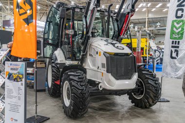 Avrupa belediye taşımacılık fuarında sergilenen beyaz endüstriyel traktör, çeşitli eklentiler ve siyah lastikler, iç mekan ayarları, olası inşaat veya Kyiv, Ukrayna - 14 Ekim 2025