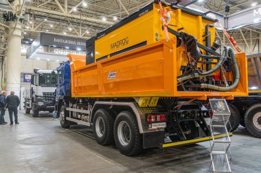 Kapalı alanda endüstriyel ortam, büyük sarı ağır yük kamyonu, eklentileri, beton döşemesi, yapay aydınlatma, koyu renk elbiseli insan figürü Kyiv, Ukrayna - 14 Ekim 2025