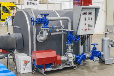 Eğri gövdeli endüstriyel makine, koyu renk, borular, mavi bileşenler, kontrol paneli, bakım malzemeleri, endüstriyel çevre, beton zemin, artifi Kyiv, Ukrayna - 14 Ekim 2025