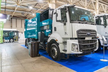 Ön planda mavi bir İskandinav çöp kamyonu ve diğer büyük ticari kamyonların sergilendiği kapalı sanayi fuarının zemininde Kyiv, Ukrayna - 14 Ekim 2025