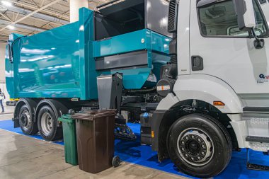 Endüstriyel atık toplama kamyonu mavi, ağır yapılı, bitişiğindeki küçük çöp tenekeleri gri çöp tenekesi, ahşap kutu.