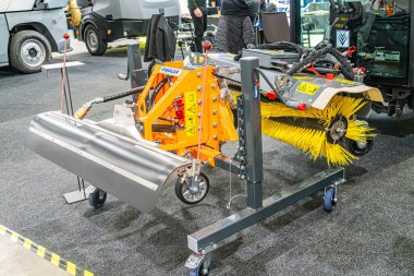 Bir atölye ortamında turuncu endüstriyel yol temizleme makinesi, sağlam metal yapı, kesme aleti eklentisi, fayanslı zemin, yapay ışıklandırma, insan ac Kyiv, Ukrayna - 14 Ekim 2025