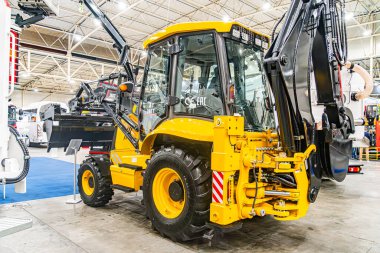 İki sarı forklift ve siyah bir kazıcı içeren kapalı endüstri sahnesi Çelişkili renkler, simetrik kompozisyon, yumuşak yapay ışıklandırma ve yüksek tavan Kyiv, Ukrayna - 14 Ekim 2025