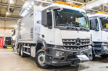 İki beyaz Mercedes-Benz ticari kamyonu kapalı, sergi salonu veya depo seti, üstten aydınlatma, endüstriyel döşeme, açılı perspektif, ön ızgara, Mercedes Kyiv, Ukrayna - 14 Ekim 2025