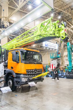 Turuncu ve sarı endüstriyel sergi. Kamyon vinci var. Arka planda makineler var. Beton zemin aşınma izleri gösteriyor.