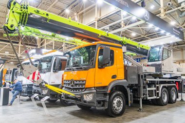 İki endüstriyel araç, biri turuncu aksanlı vinç kamyonu, diğeri turuncu aksanlı teslimat minibüsü, Kyiv, Ukrayna 'daki geniş bir depoda park edilmiş, 14 Ekim 2025