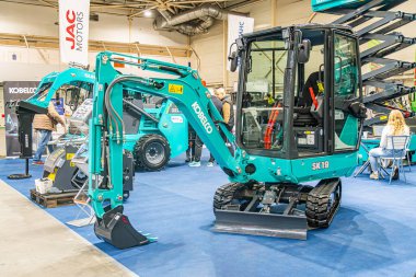 Geniş yeşil tırtıl pist yükleyicisi ve daha küçük yük traktörü mavi zemin ve tarafsız duvarları Kyiv, Ukrayna - 14 Ekim 2025