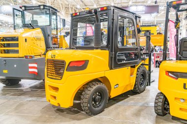 Bir endüstriyel depo ortamında üç forklift, boyutları ve tasarımları farklı siyah lastikli sarı renk, yapay aydınlatma Kyiv, Ukrayna - 14 Ekim 2025