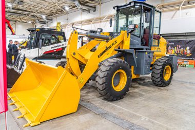 Büyük sarı kazıcı, endüstriyel bir serginin duvarına karşı diğer inşaat ekipmanlarını arka planda görünür hale getiriyor. Keskin gölgeler ve parlak aydınlatma Kyiv, Ukrayna - 14 Ekim 2025