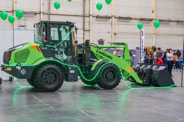 Canlı yeşil bir zirai traktör, yüksek yer temizliği ve geniş lastiklerle kapalı alanda sergileniyor. Traktörün ön yükleyicisi var, Kyiv, Ukrayna - 14 Ekim 2025