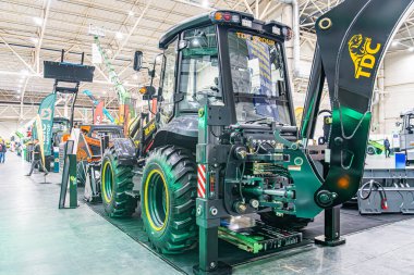 Canlı bir endüstriyel sergide biri yeşil ve sarı, diğeri siyah ve sarı olmak üzere iki büyük traktör geniş pencerelerin yakınındaki ahşap platformlarda sergileniyor.