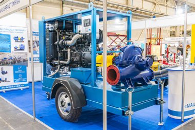 Sanayi ortamında büyük mavi motor, sarı çatılı bir yapıya karşı görüntülendiğinde birden fazla bileşen, tekerlek, silindir, boru ve valfler ortaya çıkar Kyiv, Ukrayna - 14 Ekim 2025