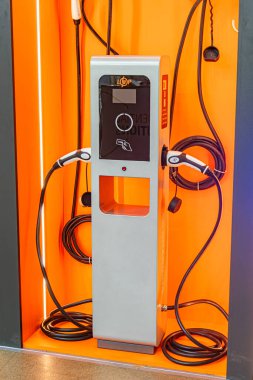 Minimalist sanayi ortamında birbirine bağlı iki kabloyla turuncu ve siyah şarj istasyonu, yapay olarak Kyiv, Ukrayna - 14 Ekim 2025