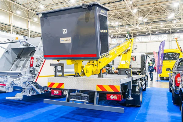 Gri gövdeli ve sarı kollu bir ticaret fuarında endüstriyel makine sergileniyor. Uyarı işaretleri, büyük lastikler, yüksek tavan, mavi zemin, ek makineler I Kyiv, Ukrayna - 14 Ekim 2025