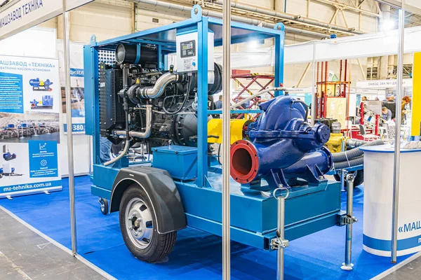 Sanayi ortamında büyük mavi motor, sarı çatılı bir yapıya karşı görüntülendiğinde birden fazla bileşen, tekerlek, silindir, boru ve valfler ortaya çıkar Kyiv, Ukrayna - 14 Ekim 2025