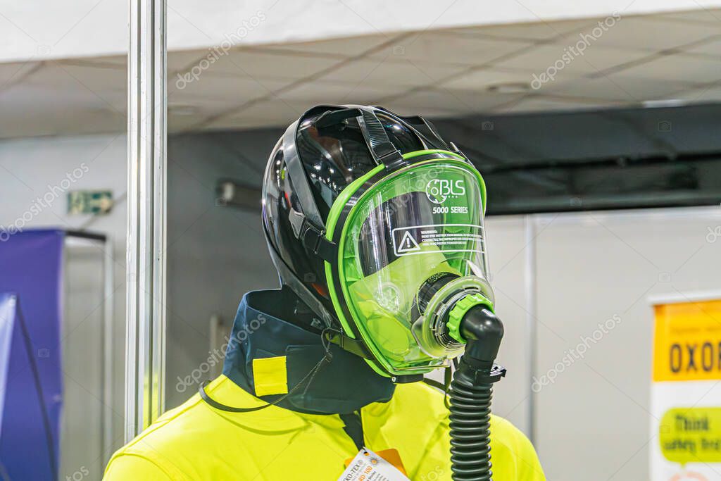 Indoor industrial setting, person in protective gear black helmet, yellow vest, respiratory device, working in potentially hazardous environment, bright artificial Kyiv, Ukraine - October 14, 2025