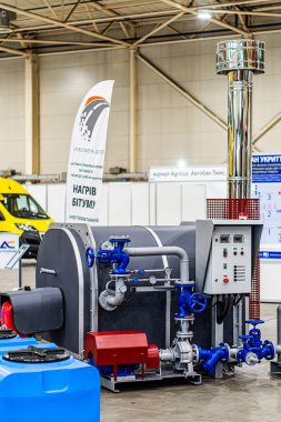 Kırmızı tekerlekler üzerinde büyük siyah ve gümüş renkli silindirik bir cihaz bitişikteki endüstriyel sergi, sarı bir minibüs ve siyah sırtında beyaz bir yazı olan Kyiv, Ukrayna - 14 Ekim 2025