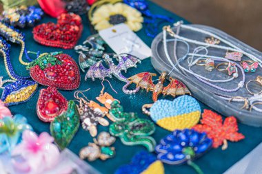 Bir Ukrayna fuarında boncuklu mücevher sergisinde çeşitli küpe desenleri, yapraklar, çiçekler, canlı renkte kalpler kırmızı, yeşil, mavi, sarı aranjman Kyiv, Ukrayna - 20 Eylül 2025