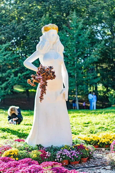 Kyiv, Ukrayna 'da 20 Eylül 2025' te büyük bir saksıda saksılarda çiçek açan gür yeşillik ve ağaçlarla kısmen gizlenmiş, stilize edilmiş bir insan figürü heykeli.