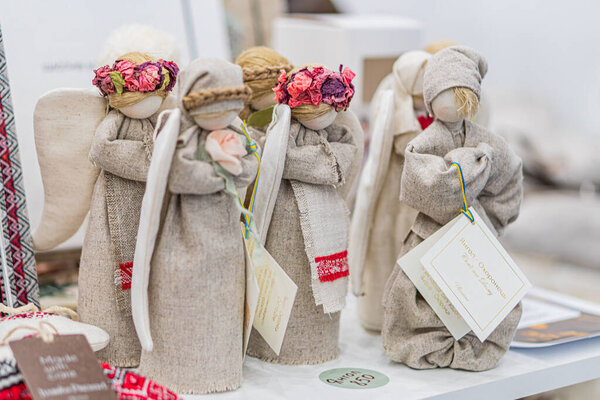 Три мешковатых ангела на белом столе на украинской ярмарке, отчетливо украшенные красными, розовыми и зелеными элементами