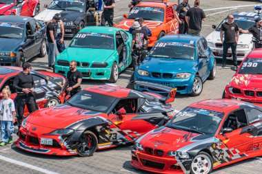 Kyiv Araba Sürükleme Festivali Üç kırmızı yarış arabası 60, 18, 23 asfalt kaputlar üzerinde bir çukur alanına dizilmiş Motorlar göstermektedir Sponsor çıkartmaları her arabayı süslüyor Kyiv, Ukrayna 06-15-2025