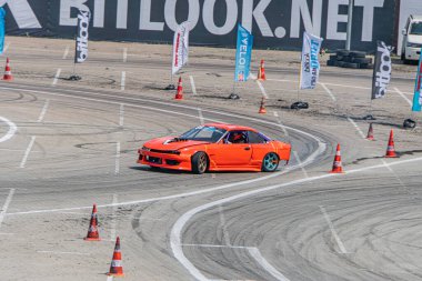 Turuncu BMW, Kyiv Araba Sürükleme Festivali sırasında toprak yolda sürükleniyor. Topraksı kahverengi yarış pisti ve turuncu trafik konileri Kyiv, Ukrayna 06-15-2025