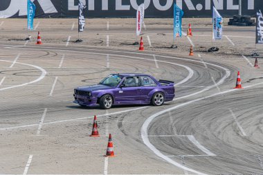 Mor BMW araba toprak yolda sürükleniyor, turuncu koniler tarafından işaretlenmiş arka plandaki bulanık manzara hız ve hareketi Kyiv, Ukrayna 06-15-2025