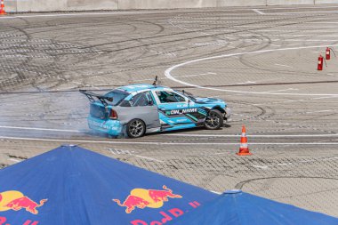 Kyiv Araba Sürükleme Festivali sahnesi gri pistte hasarlı mavi ve siyah BMW araba enkazı, turuncu güvenlik konileri ve Ukrayna, 06-15-2025 Red Bull şemsiyesi