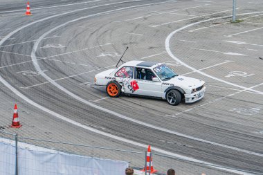 Kırmızı aksanlı beyaz bir BMW 'nin yakın çekimi Kyiv Araba Sürükleme Festivali sahnesinde bir sürücü miğfer takıyor, turuncu koniler Kyiv, Ukrayna 06-15-2025