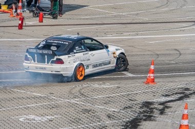 Kyiv Araba Sürükleme Festivali 'nde sürüklenen beyaz BMW arabası Smoky, arka planda beyaz işaretli ve turuncu koni yüksek görüş alanı olan siyah asfalt yoluna döndü. Na Kyiv, Ukrayna 06-15-2025