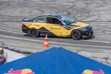 Sarı BMW arabası yarış pistinde sürükleniyor, arka planda kırmızı çadır var, Kyiv, Ukrayna 06-15-2025 etkinliklerinde yer alan iki kişi